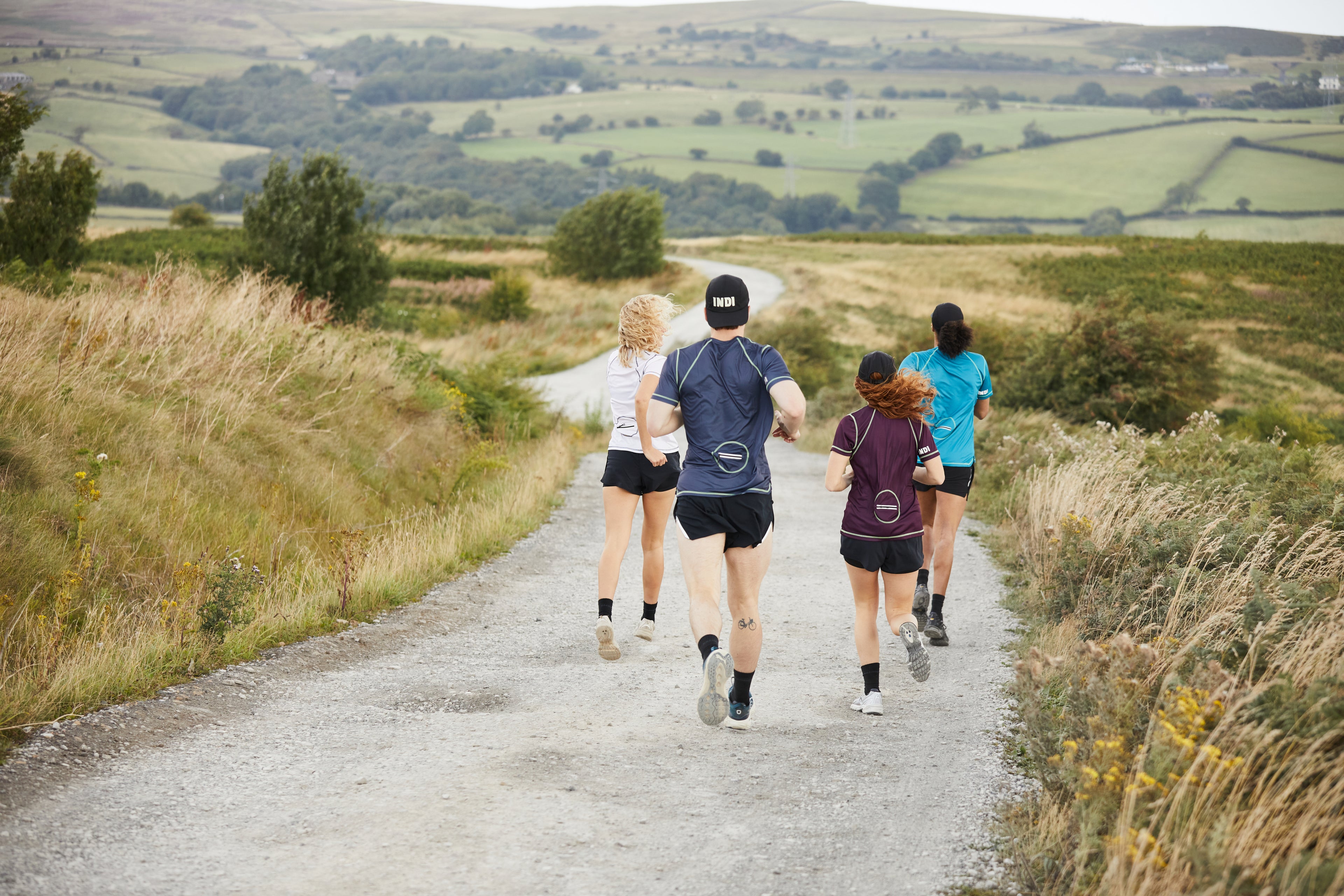 A photograph taken from behind of four runners running down a rural road