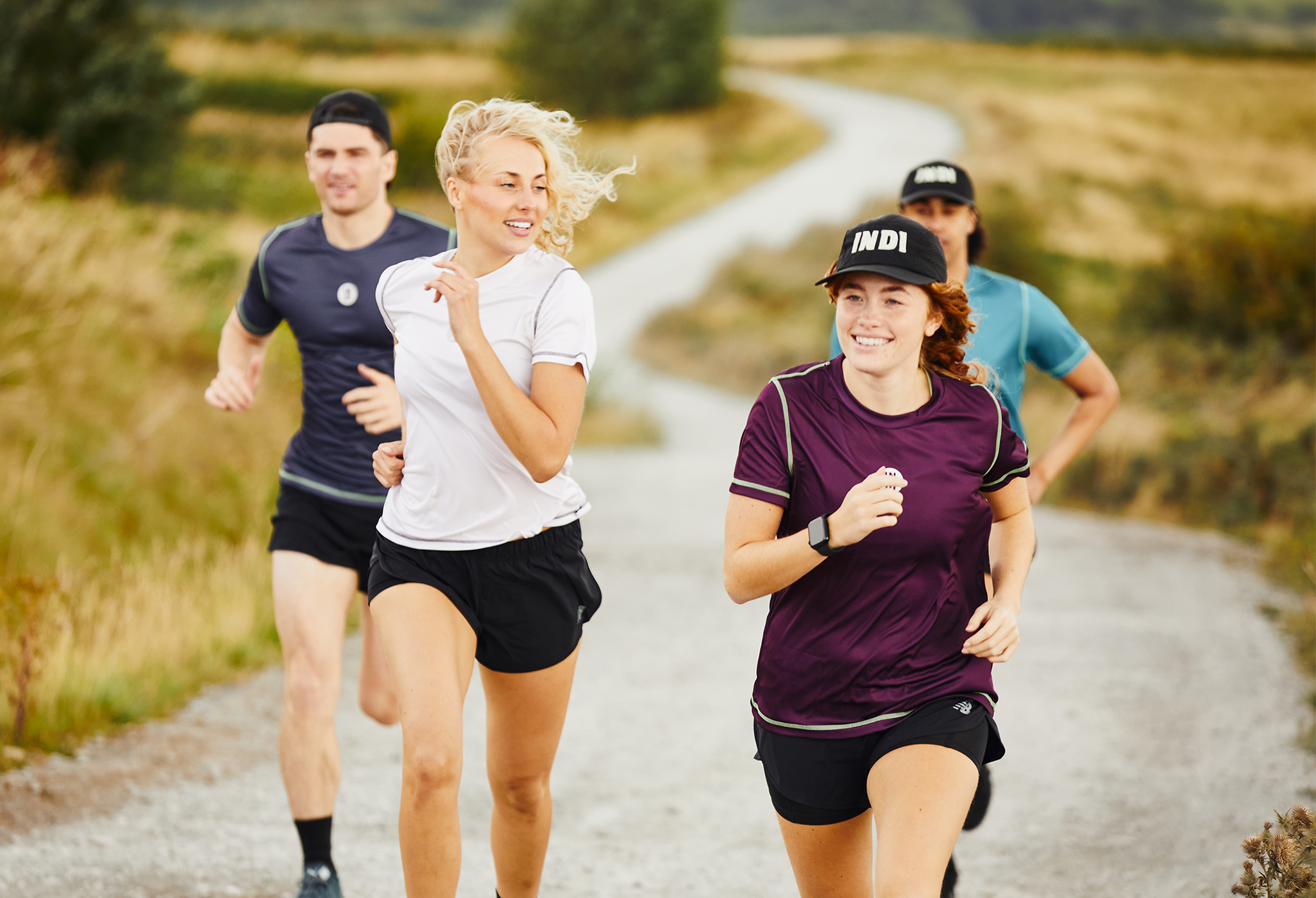 Two women runners in the foreground with the two men running behind them. All on a winding country road with the road in view behind them